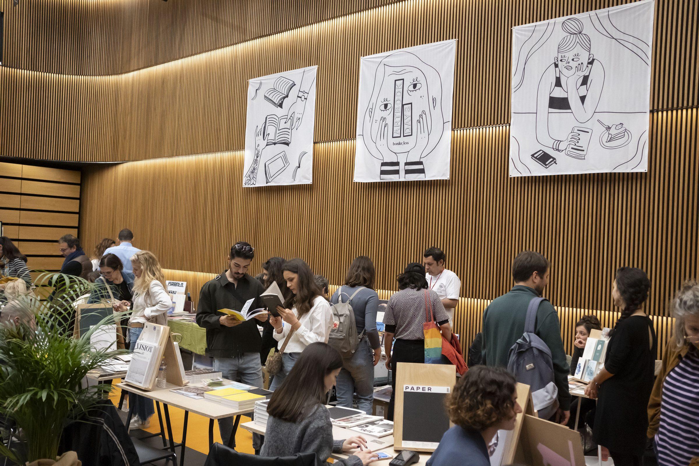 Ahşap duvarlı salonda kalabalık sanat kitabı fuarı