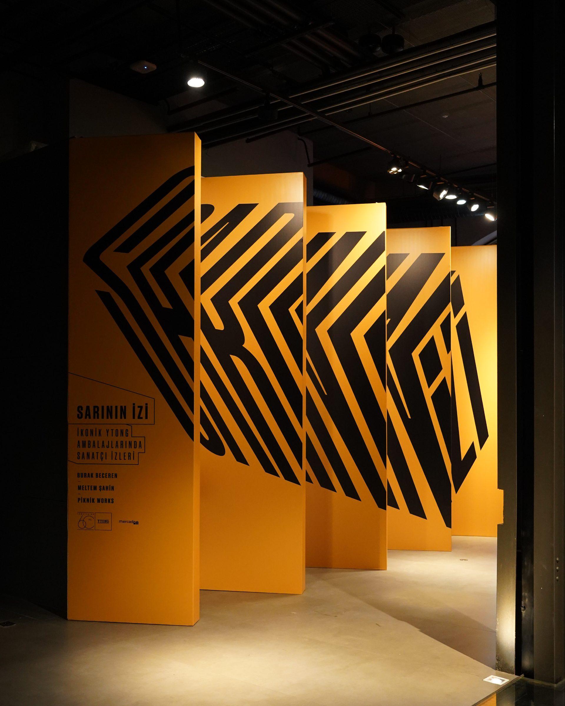 Siyah zikzak grafikli turuncu panellerden oluşan sergi yerleştirmesi