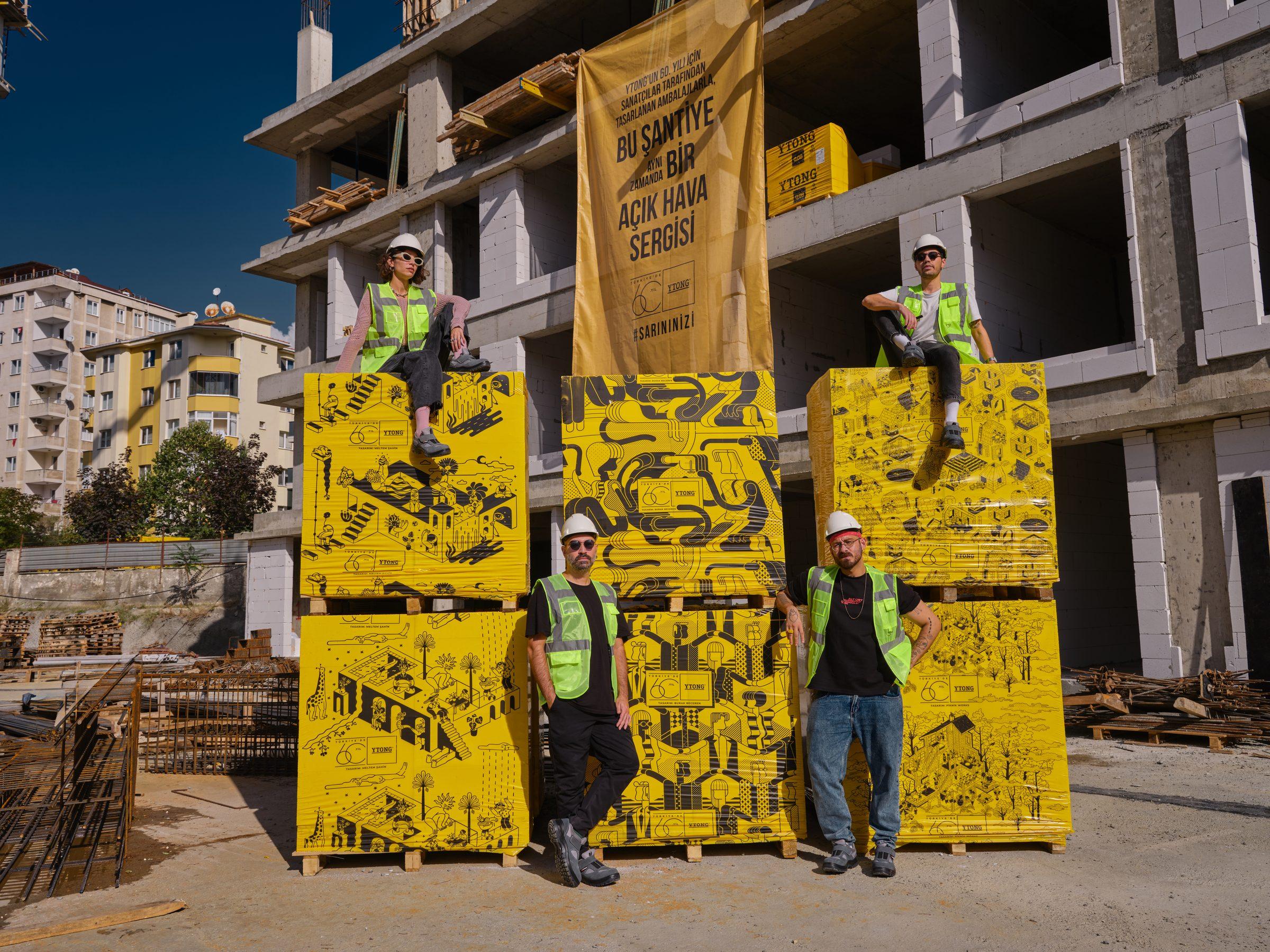 İnşaat halindeki bir binanın önünde sarı desenli bloklar ve üzerlerindeki kişiler